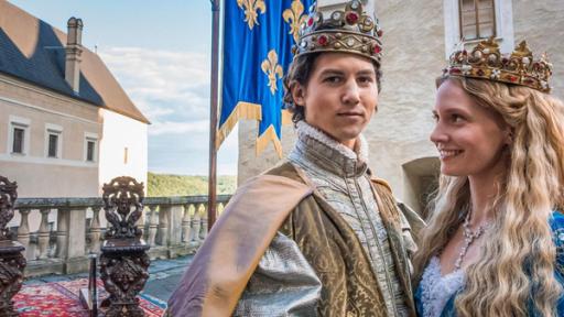 Auf der Terasse eine Schlosses stehen zwei Throne auf einem roten Teppich. Im Vordergrund zu sehen sind Endres, gespielt von Schauspieler Tim Oliver Schultz, und Prinzessin Leonora, gespielt von Frida Lovisa Hamann. Beide haben prächtige Gewänder an und tragen Kronen auf dem Haupt.