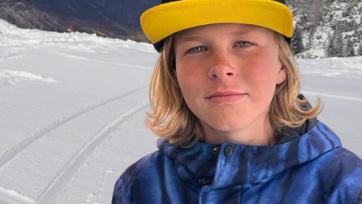 stark! - Teaser - Lan - Freestyle auf Skiern | Rechte: ZDF Lan schmunzelt in die Kamera. Er hat blaue Augen, Sommersprossen und langes, blondes Haar. Er trägt eine blaue Winterjacke und eine Baseballmütze mit gelbem Schild. Im Hintergrund sieht man eine verschneite Piste