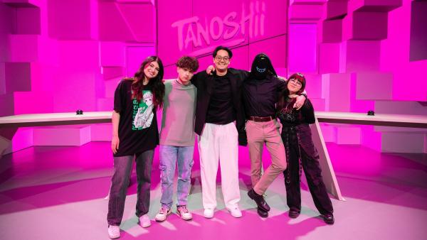 Im Tanoshii-Studio stehen Mahluna, Milo, Moderator Raafey, Drawinglikeasir und Johanna hinter ihren Pulten. Hinter ihnen ist eine pinke Studiokulisse und oben mittig das Tanoshii-Logo