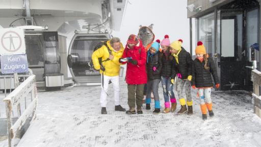 Rechte: KiKA/MingaMedia Schneewanderung in den Alpen. Singa, Volker Rosin und die TanzAlarm-Kids marschieren munter durch das verschneite Gelände und sehen nicht, wie sich der TanzTapir, angelockt von beschwingter Hüttenmusik, von der Truppe entfernt.