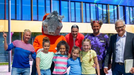 Rechte: KiKA/ZDF/Ron Bergmann Moderatorin Singa, TanzTapir, die TanzAlarm-Kids, Kindermusiker Anton, Witzbold Tom Lehel und der Schuldirektor stehen lächelnd vor der Schule.