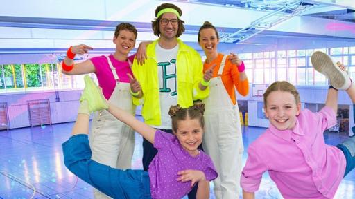Rechte: KiKA/ZDF/Ron Bergmann Die TanzAlarm-Kids stehen in sportlichen Posen vor Kindermusiker herrH und seinen Tänzerinnen mitten in der Sporthalle. TanzTapir steht rechts an der Seite mit einem Kletterseil in der Hand.