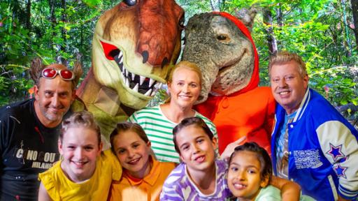 Rechte: KiKA/MingaMedia/Ron Bergmann Tom Lehel, ein T-Rex, TanzTapir, Singa, Kindermusiker Volker Rosin und die TanzAlarm-Kids stehen mitten im Wald unfd lächeln in die Kamera.