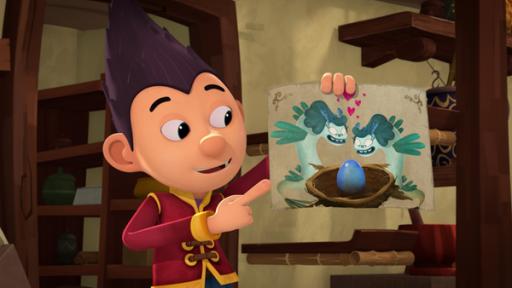 Rechte: KiKA/Flying Bark Productions Pty Ltd. Tashi hält ein bemaltes Blatt Papier hoch und zeigt mit dem Finger darauf. Es ist ein Ei zu sehen, das von zwei schlangenähnlichen Kreaturen, sogenannten Wolkensirenen, angeschaut wird.