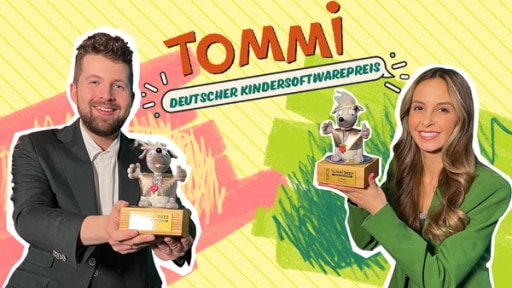 Recht steht Tim in einem dunklen Anzug gekleidet mit einer kleinen Hundefigur in der Hand. Links steht Soraya in einem grünen Anzug gekleidet mit einer kleinen Hundefigur in der Hand. In der Mitte ist ein Schriftzug: TOMMI - Deutscher Kindersoftwarepreis.