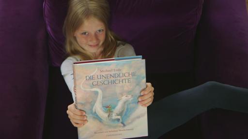 Buchtesterin Anna hält das Buch "Die unendliche Geschichte" in die Höhe.