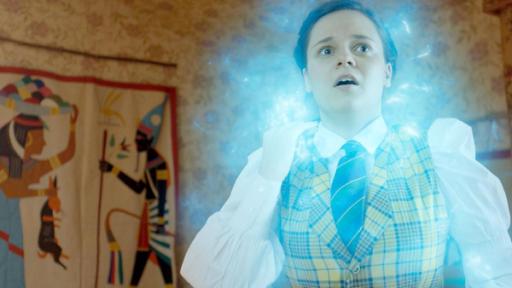 Theo ist umgeben von blau-weißem, magisch-leuchtendem Licht. Sie steht in ihrem Zimmer und sieht erschrocken aus.