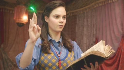 Doppelter Ärger | Rechte: 2022 Cottonwood Media – ZDF – ZDF Studios Theodosia (Eloise Little) spricht eine Beschwörungsformel, die aus dem aufgeschlagenen Buch stammt, das sie in ihrer linken Hand hält. Mit ihrer rechten Hand macht sie das Heka-Handzeichen zur Beschwörung der Magie. Ein grüner Funken leuchtet über ihrer Hand auf. Ihr Blick geht gebannt und konzentriert nach vorne.
