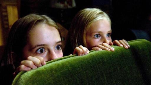 zwei Mädchen fürchten sich und verstecken sich hinter einem Sofa