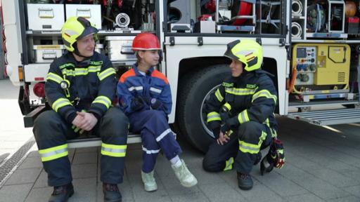 Thandi und Feuerwehrmitarbeiterinnen sitzen vor einem Feuerwehrauto