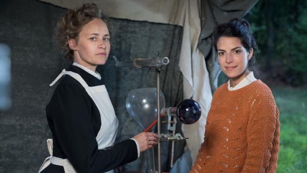 Clarissa (rechts) steht neben Marie Curie (Inez Bjørg David, links). In der Mitte steht ein Röntgengerät.