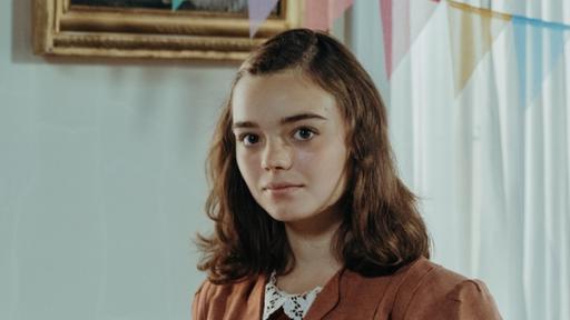 Rechte: KiKA/Sabine Finger Clarissa trifft auf Anne Frank (Katharina Kron). Clarissa lächelt und hat einen alten Fussball in der Hand. Anne Frank schaut neutral und hält ein Buch in ihren Händen.