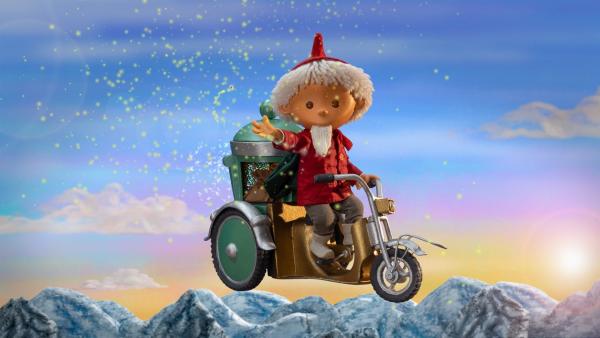 Der Sandmännchen fliegt auf einem Motorroller und verstreut Traumsand. Hinter ihm ist ein Himmel mit Sonnenuntergang über Gebirgsgipfeln.