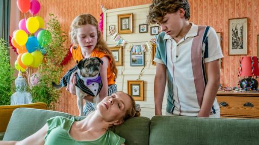 Die Tiefschlaf-Spindel | Rechte: ZDF/Mideu Films/Steffen Junghans Tief in Dornröschen-Schlaf versunken liegt Olivia (mitte links) auf ihrer Wohnzimmercouch. Patty (links) beugt sich über sie und hält dabei eine schwarz-weiß gemaserte, kleine Bulldogge in Smoking und lila Fliege in den Händen. Offenbar möchte Patty, dass der Hund Olivia küsst. Jan steht rechts daneben, beobachtet die Szene und zieht dabei ein Gesicht, das alles andere als Optimismus ausstrahlt.