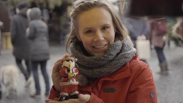 Reporterin Elisabeth hält einen Figur eines Weihnachtsmannes in den Händen, der Saxophone spielt.